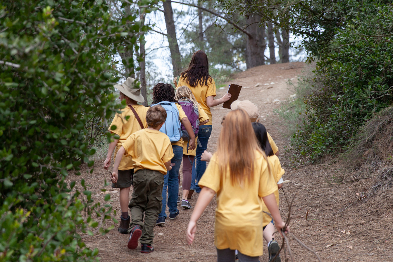 Summer camp counselor leading kids on nature hike on trail in woods